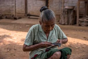 vieille dame en train de tailler des pics à brochette dans le village